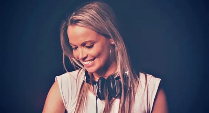 Adrelina smiling behind the decks, headphones around her neck